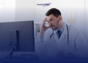 Tired male doctor sitting at a computer, holding his head while writing notes, with HealthOrbit logo in the background